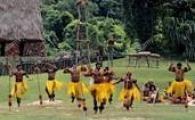 A group of men wearing grass skirts perform meke, a traditional Fijian dance.