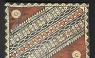Masi, a bark cloth, has a brown background in the top and bottom corners and a horizontal pattern of repeated squares and linked chains in between the brown. 