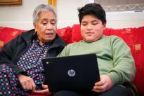Older woman and a child sitting together looking at computer on child's lap.